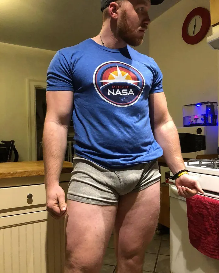 Homme barbu en t-shirt bleu Rogue NASA et sous-vêtements gris, debout dans une cuisine.