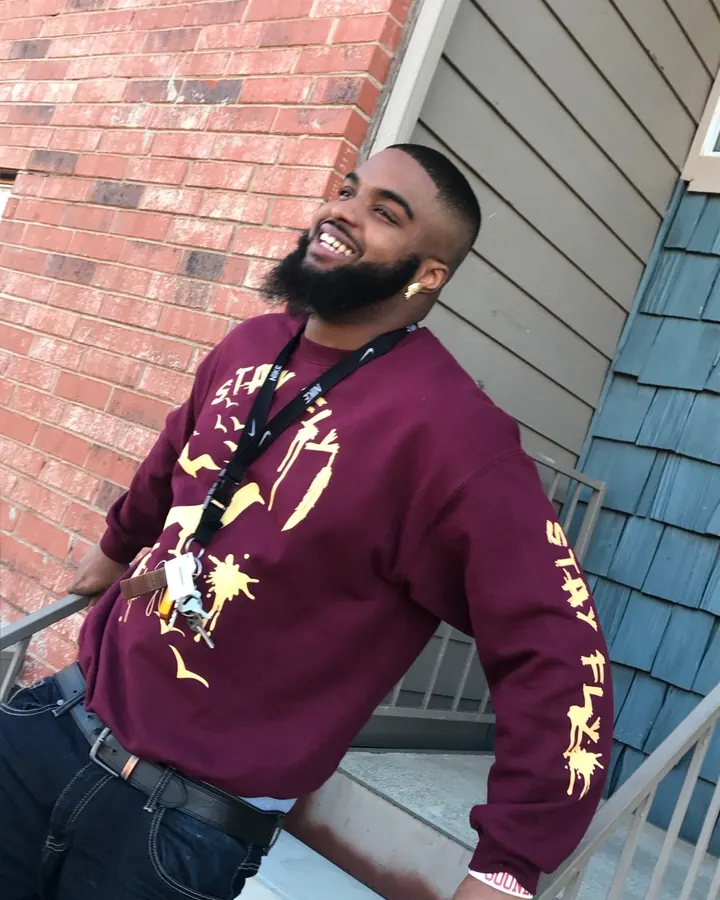 Homme africain en t-shirt gris, barbe, prenant un selfie dans un miroir, regard concentré, lumière neutre, expression calme.