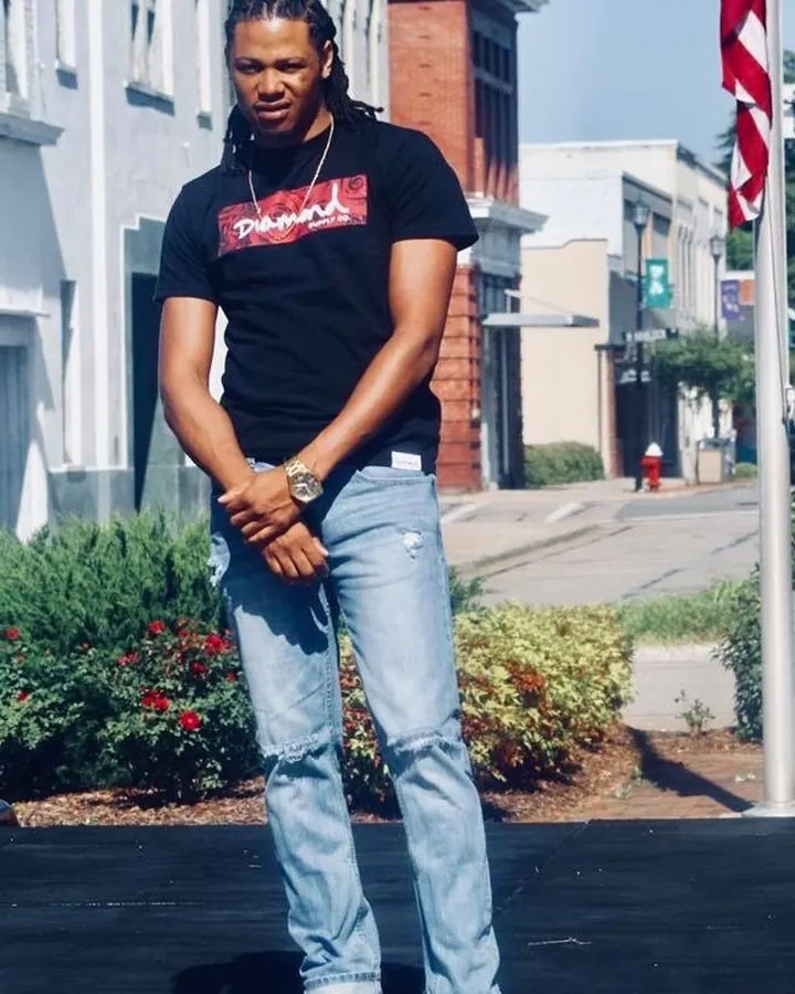 Homme torse nu, peau foncée, dreadlocks, t-shirt noir 'Diamond', jeans déchirés, regard vers le bas.