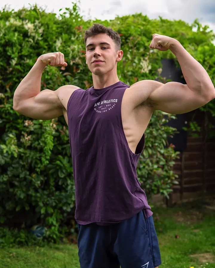 Jeune homme torse nu, peau blanche, cheveux bruns courts, flexion des bras, t-shirt violet 'APE ATHLETICS', jardin.