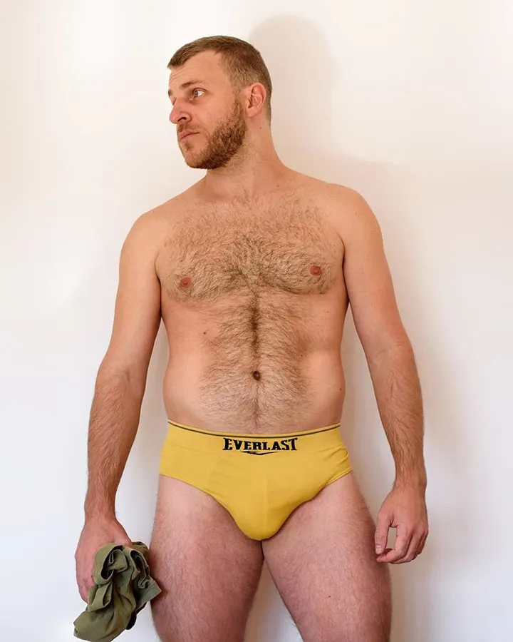 Homme torse nu, barbe courte, sous-vêtement jaune Everlast, tenant un morceau de tissu vert.