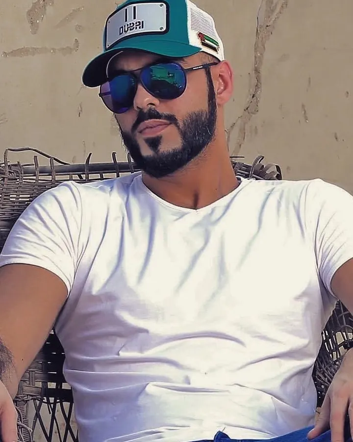 Homme en casquette verte et blanche, lunettes de soleil, t-shirt blanc, assis sur une chaise en osier.