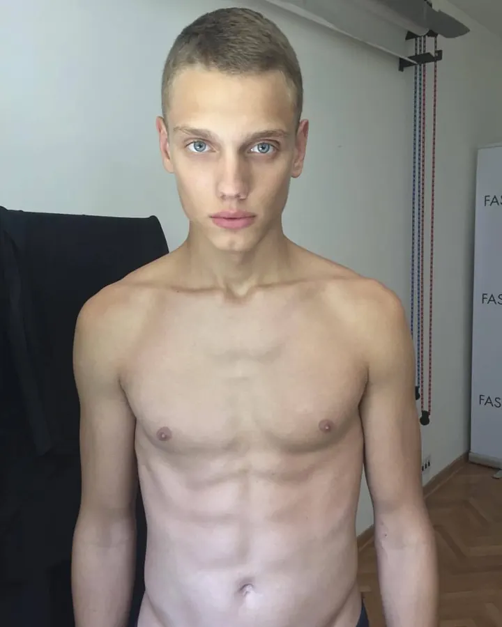 Homme torse nu en sous-vêtements noirs, faisant un geste de poing fermé.