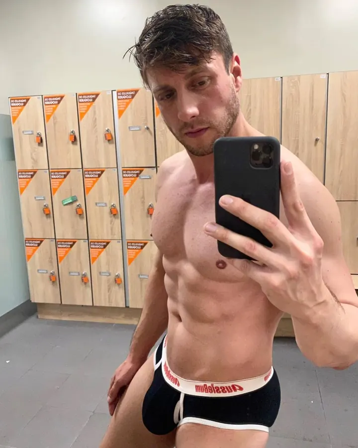 Homme torse nu, prenant un selfie dans une salle de sport, sous-vêtements noirs et blancs
