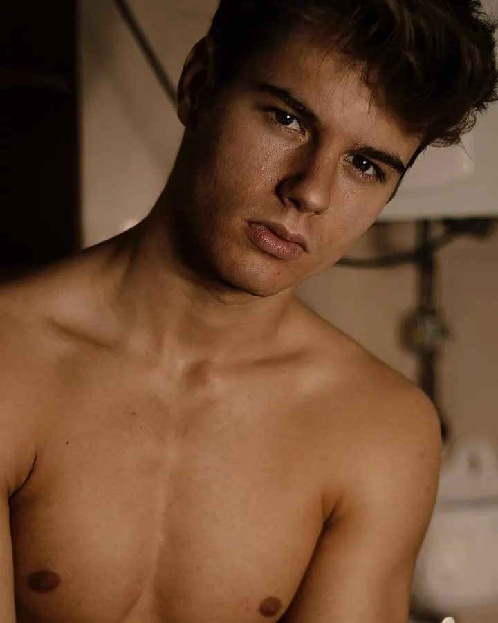 Jeune homme latino torse nu, regard intense, dans une lumière chaude en intérieur