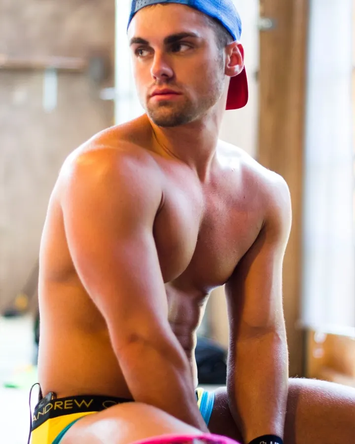 Homme torse nu, en sous-vêtements, regard intense contre un fond gris.