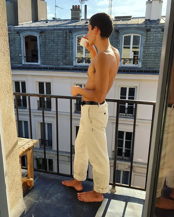 Homme torse nu, en sous-vêtements, regard intense contre un fond gris.