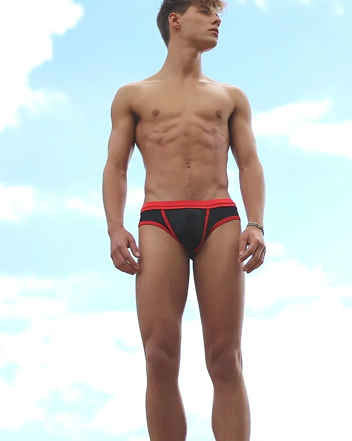 Homme torse nu, en sous-vêtements, regard intense contre un fond gris.