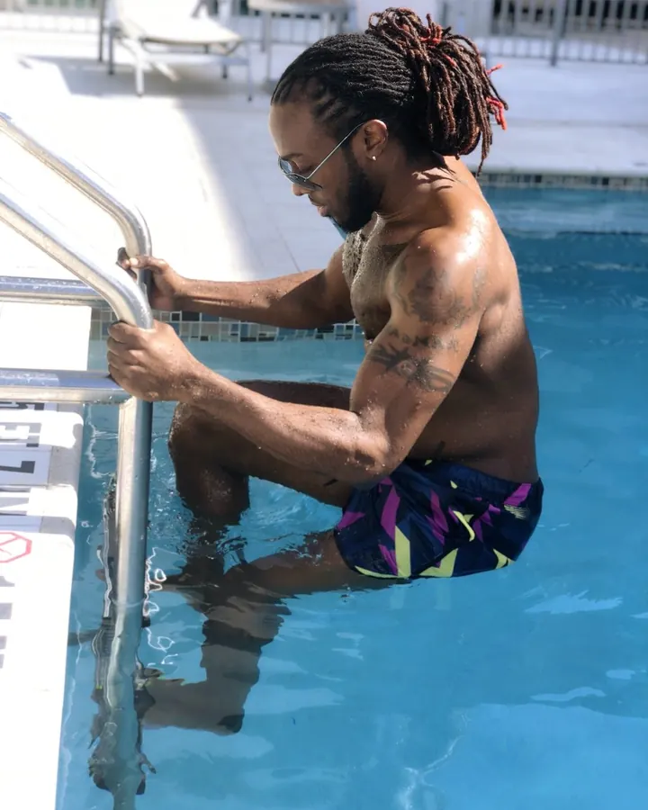 Homme musclé, torse nu, sortant d’une piscine, dreadlocks, lunettes de soleil, short coloré.