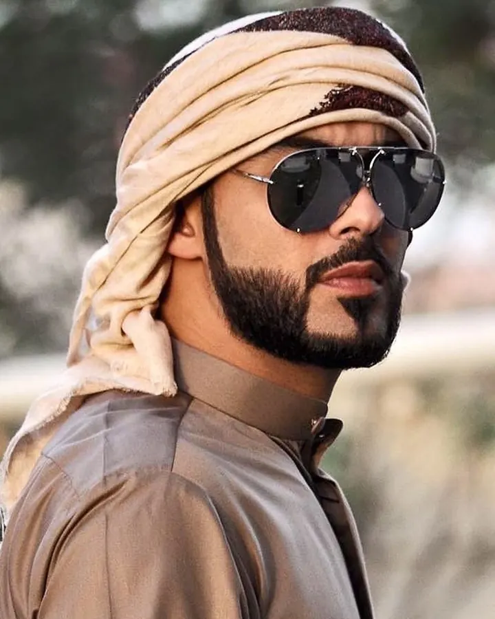 Homme arabe portant un turban beige et des lunettes de soleil noires, regard intense