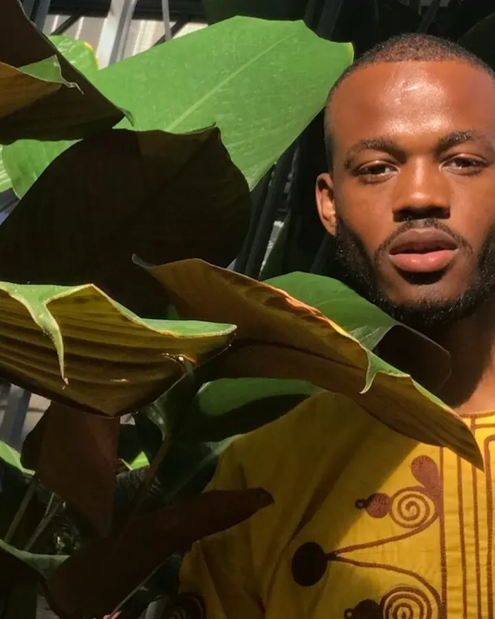 Homme africain de 25 à 35 ans, torse nu, portant un t-shirt blanc, sous-vêtement Calvin Klein, devant un rideau jaune.