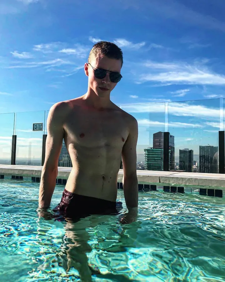 Homme européen de 18 à 25 ans, torse nu, portant un t-shirt blanc, sous-vêtement Calvin Klein, devant un rideau jaune.