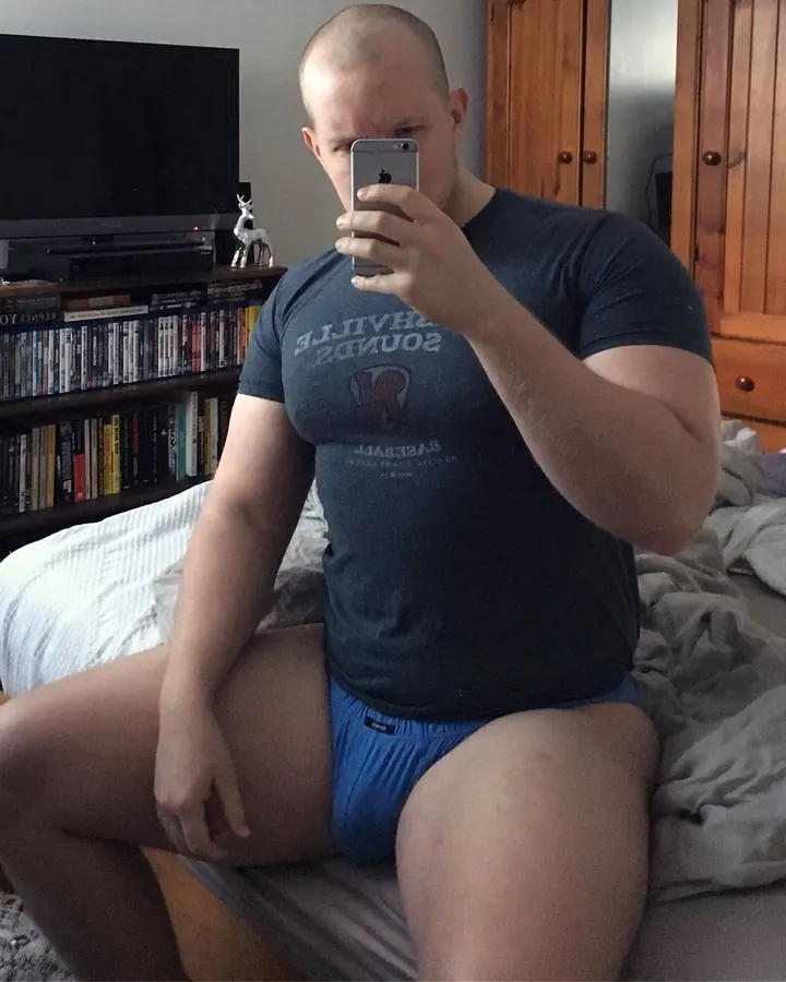 Homme européen torse nu, gros, en sous-vêtements bleus, posant devant un fond blanc.