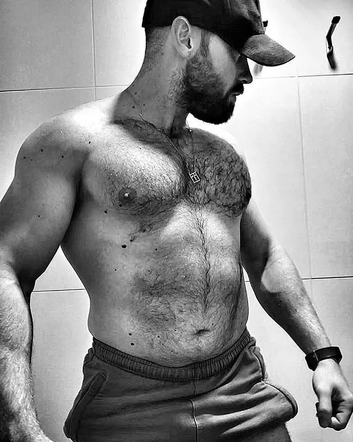 Homme européen torse nu, musclé, en sous-vêtements noirs, posant dans une salle de bains carrelée.
