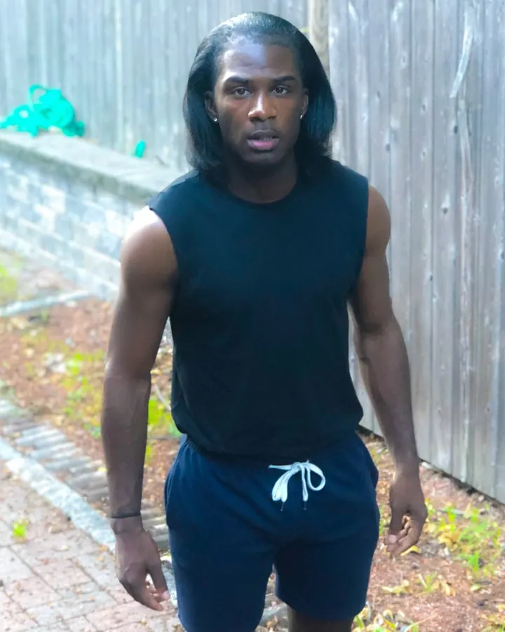 Homme africain torse nu, musclé, en sous-vêtements noirs, debout devant un mur en bois.