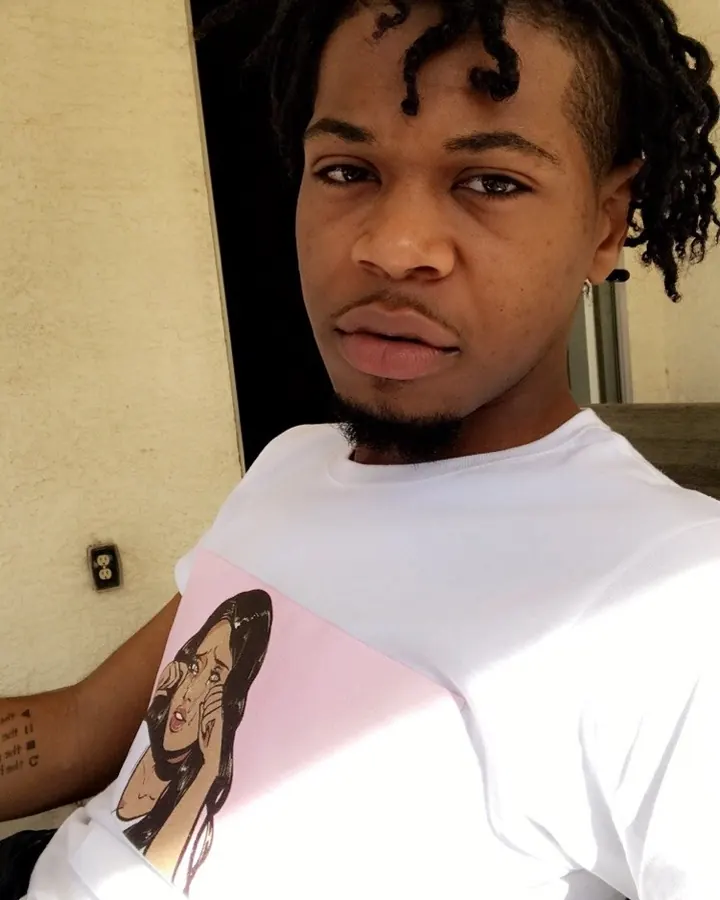 Homme africain en t-shirt blanc avec imprimé, regardant directement l'appareil photo, en extérieur.