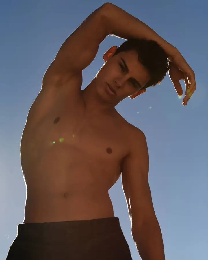 Homme torse nu, debout, regardant directement l'appareil photo, avec une main sur la hanche.