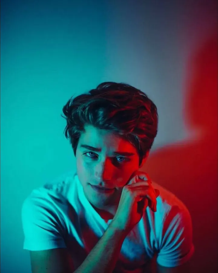 Homme torse nu, regardant directement l'appareil photo, avec une lumière bleue et rouge sur le visage.