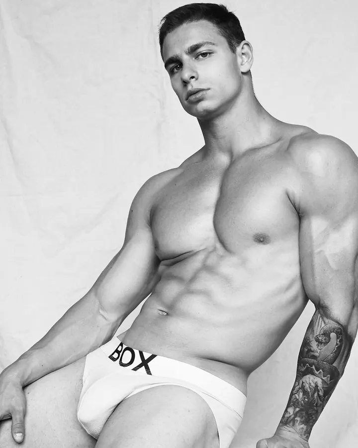 Homme torse nu, debout, regardant directement l'appareil photo, avec une main sur la hanche.