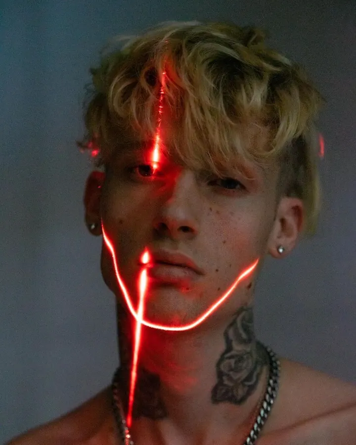 Homme torse nu, regardant directement l'appareil photo, avec une lumière rouge sur le visage et un tatouage visible sur le cou.