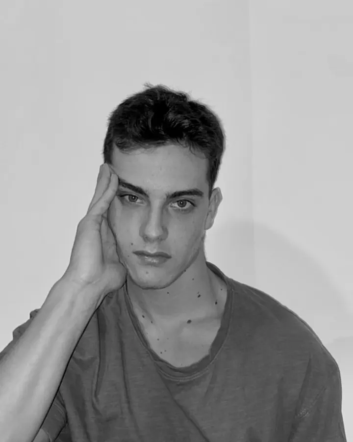 Portrait en noir et blanc d'un jeune homme aux cheveux courts, regardant l'objectif, la main posée sur sa tempe.