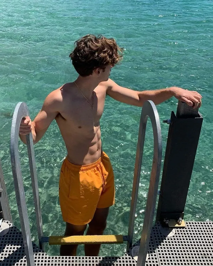 Jeune homme torse nu, aux cheveux blonds, regardant vers le haut, main sur la tête, lumière vive derrière lui